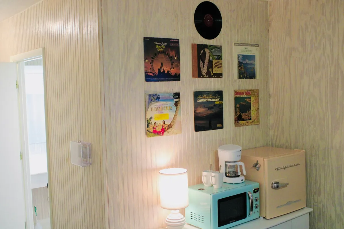 A warm, inviting scene with a retro coffee maker and a pastel-colored microwave prominently displayed alongside vintage vinyl records and soft lamp light. The setup hints at both culinary convenience and a relaxed, homey atmosphere, perfect for sipping coffee while enjoying music or conversation.