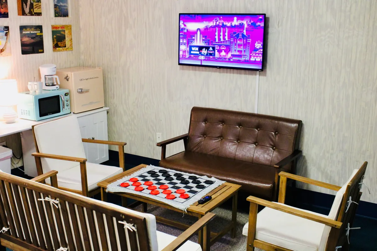 A relaxed living area with a checkerboard table set for games, a plush brown leather sofa, and a flat-screen TV, all set in a calm, welcoming space. The layout encourages socializing, lounging, and entertainment for guests of all ages.